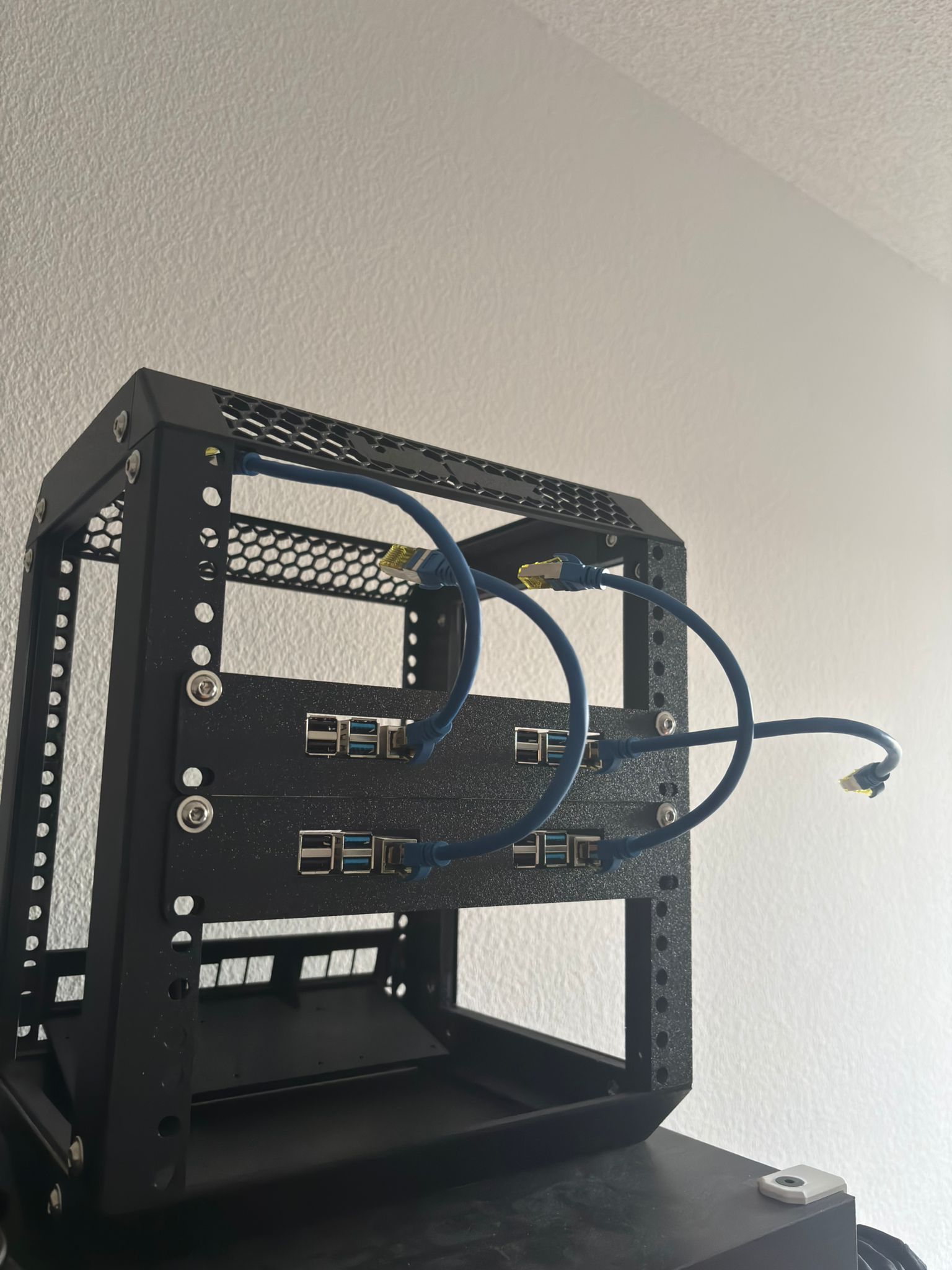 Das schwarze 10-Zoll-Rack von hinten mit zwei übereinanderliegenden Shelfs, darauf vier Raspberry Pis, deren Netzwerkbuchsen mit kurzen blauen Patchkabeln belegt sind.
