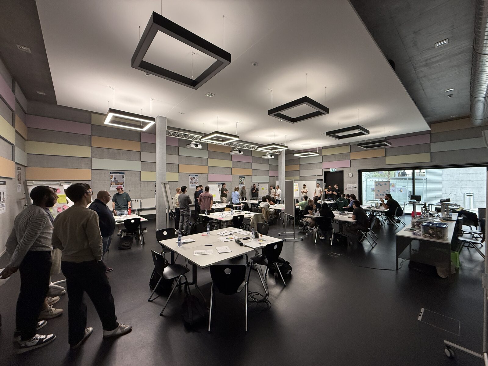 Blick in den grossen Arbeitsraum mit vielen Gruppentischen, Stellwänden und Post-its an den Wänden.