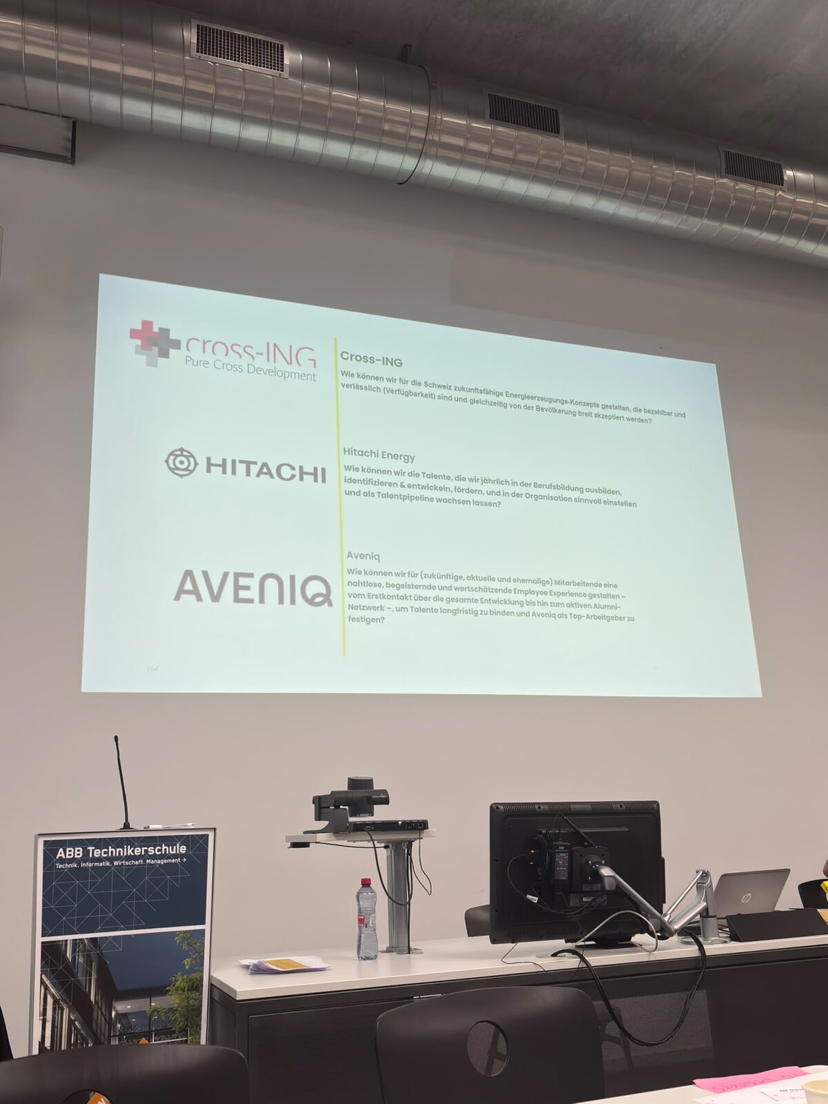 Projizierte Folie mit den drei Firmen-Challenges von cross-ING, Hitachi Energy und Aveniq nebeneinander.