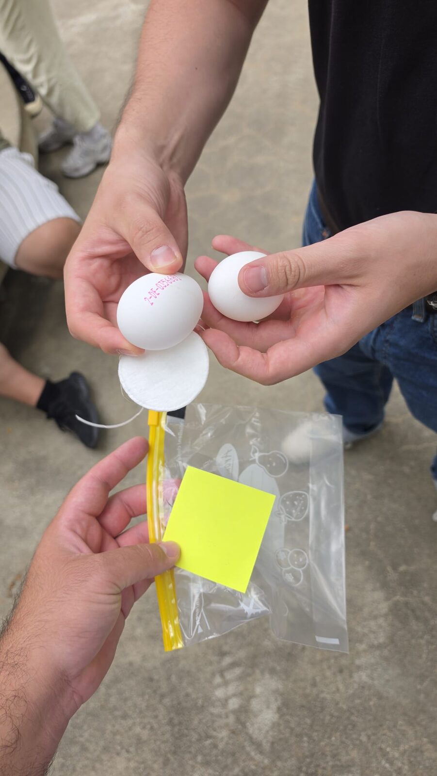 Mehrere Hände halten einen Prototyp aus Tischtennisbällen, einem gelben Halm und einem Post-it.