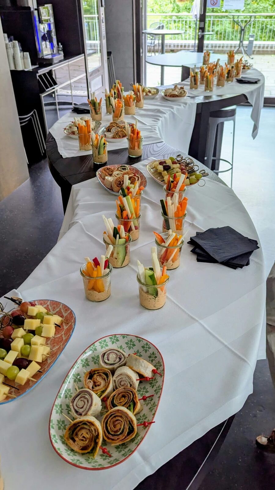 Das Apérobuffet mit Gemüsesticks in Gläsern, Käsewürfeln und Wraps auf weiss eingedeckten Tischen.